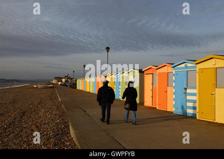 Menschen zu Fuß vorbei an Linie der hölzernen Umkleidekabinen am Meer auf eine Winter-Nachmittag, Seaford, East Sussex, England Stockfoto