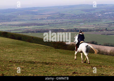 Frau, die im Winter auf einem weißen Pferd entlang des Berges von South Downs in der Nähe von Firle Beacon reitet, South Downs National Park, East Sussex, England, Großbritannien Stockfoto