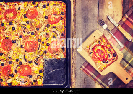 Vintage getönten hausgemachte Thunfisch Pizza mit Tomaten, Oliven, Zwiebeln und Mais auf hölzernen Hintergrund, Ansicht von oben. Stockfoto