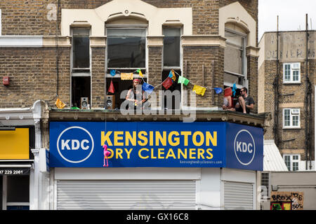 Menschen in Windows während der 50. Notting Hill Carnival feiern; Windows mit bunten Girlanden verziert Stockfoto