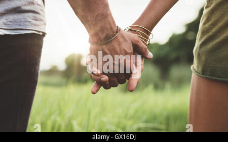 Junges Paar hand in hand durch die Wiese gehen. Schuss mit Fokus auf Händen von Mann und Frau hautnah. Stockfoto