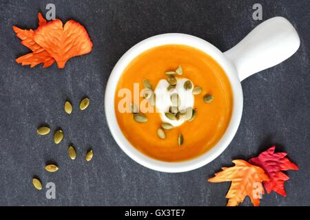 Cremige Kürbis-Suppe mit Kürbiskernen und Creme auf Schiefer Hintergrund mit Herbstlaub gekrönt Stockfoto