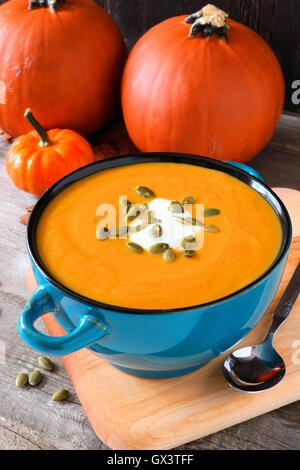 Cremige Kürbissuppe, garniert mit Samen und Sahne in eine blaue Schüssel mit Herbst Kürbisse im Hintergrund Stockfoto