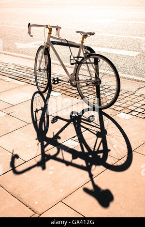 Hipster single-Gear Fixie Fahrrad gesperrt, um ein Metall-Ständer auf einem Pflaster. Große Schatten projiziert auf dem Bürgersteig. Instagram-Effekt. Stockfoto