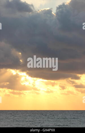 Ein wunderschön Moody Himmel mit der Sonne hinter den Wolken, bei Sonnenuntergang, mit dem Meer Stockfoto