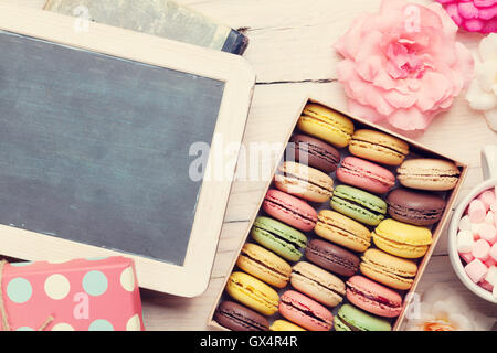 Bunte Makronen und Blackboard. Süßen Macarons in Geschenkbox auf Holztisch. Draufsicht mit textfreiraum für Ihren Text. Getönten Stockfoto