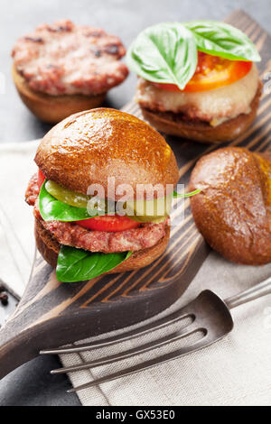 Hausgemachte Burger mit Rindfleisch, Käse, Tomaten, Gurke und Basilikum auf Schneidebrett Stockfoto