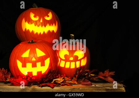 Gestapelte Halloween Jack-o-Laternen beleuchtet in der Nacht mit altem Holz und Blätter im Herbst Stockfoto