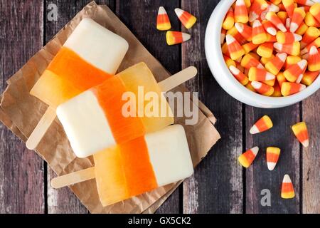 Halloween Candy Corn Eis am Stiel nach unten anzeigen auf rustikalen Holz Hintergrund mit Schale mit Süßigkeiten Stockfoto