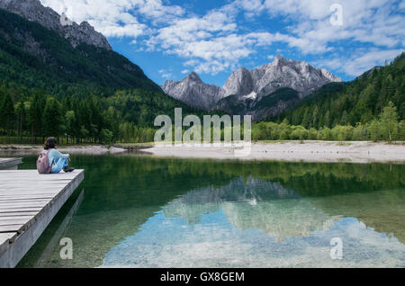 Blick auf die Julischen Alpen von Kranjska Gora mit Jasna-See und Mädchen sitzen am Pier in Slowenien Stockfoto