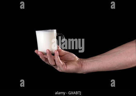Hand hält eine Tasse mit Milch auf schwarzem Hintergrund Stockfoto