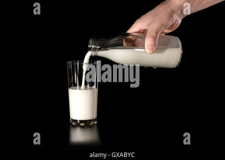 Man gießt Kuhmilch von Glasflaschen in einem Glas auf einem schwarzen Hintergrund Stockfoto