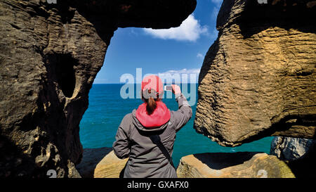 Portugal: Frau nehmen Momentaufnahme der Blick auf das Meer mit Smartphone durch ein Naturstein-Fenster Stockfoto