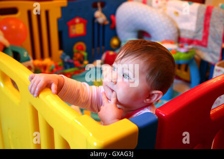 Babymädchen denken in einen bunten Laufstall Stockfoto