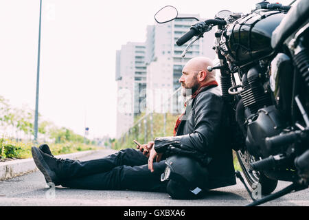 Ältere männliche Motorradfahrer sitzen am Straßenrand stützte sich auf Motorrad mit smartphone Stockfoto