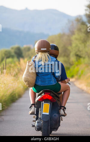 Rückansicht des jungen Paares Reiten Moped auf Landstraße, Mallorca, Spanien Stockfoto