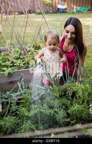 Mutter und Tochter im Garten, Bewässerung von Pflanzen zusammen mit Schlauch Stockfoto