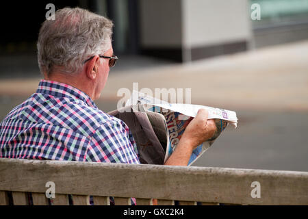 Ein älterer Mann sitzt auf einem Sommersitz Montag Post Zeitunglesen in zentralen Dundee, Großbritannien Stockfoto