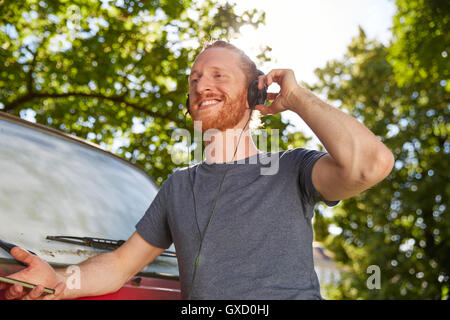 Junger Mann im Freien, mit Kopfhörern, Lächeln Stockfoto