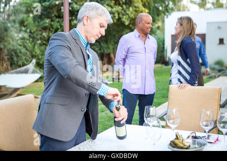 Reifer Mann uncorking Weinflasche an Gartenparty Tisch Stockfoto