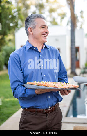 Reifer Mann hält Fischküche auf Schneidebrett auf Gartenparty Stockfoto