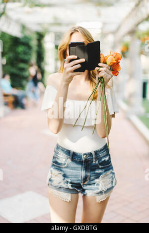 Junge Frau im Freien stehen, hält Rosen, mit smartphone Stockfoto