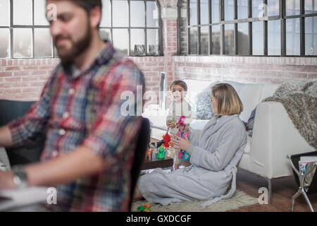 Mann, sitzend arbeiten am Schreibtisch, junge Frau mit Kleinkind hinter ihm spielen Stockfoto