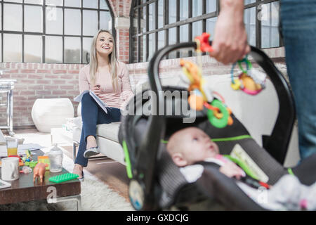 Vaters Haus verlassen, mit Baby Girl im Autositz, Mutter auf Sofa sitzen, arbeiten Stockfoto