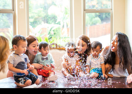 Mütter mit Babymädchen und jungen feiern mit Konfetti auf Esstisch Stockfoto