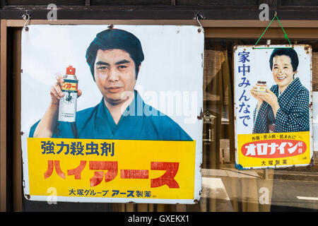 Japan, Izushi. Original 1970er Stil Zinn Werbeschilder hängenden außerhalb Schaufenster, picturing Schauspieler holding Aerosol fliegen killer Spray. Stockfoto