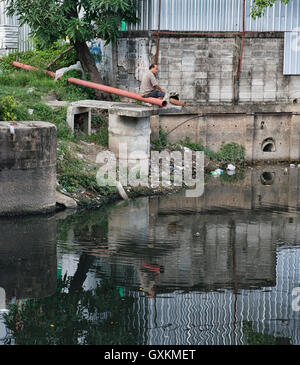 Mann sitzt auf Rohr reflektiert in den Slums von Bangkok, Thailand Stockfoto