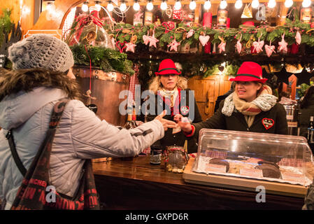 Personal an der Bar gefiederten tragen bayerische Hüte dienen Glühwein an einen Kunden in einem der vielen Holzhütten auf dem Münchner Weihnachtsmarkt Stockfoto