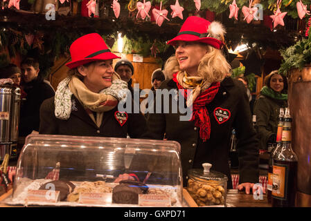 Zwei Mitarbeiter der Bar tragen bayerische gefiederten Hüte dienen Glühwein in einer der vielen Holzhütten im München Chris Stockfoto