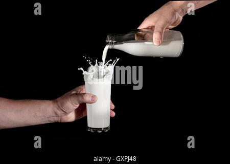 eine menschliche Hand hält das Glas, und die andere schüttet es Milch aus der Flasche auf schwarzem Hintergrund. fliegen-spray Stockfoto