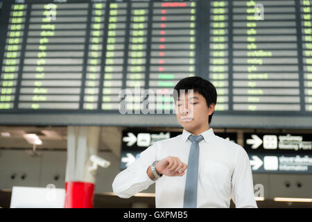 Asiatische junge Geschäftsmann Blick auf seine Uhr vor Flughafen Flugplan am Flughafen-terminal. Business Travel-Konzept. Stockfoto