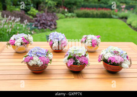 Vasen mit blühenden Blumen auf Teakholz-Tisch im Freien im Garten Stockfoto