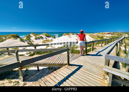 Portugal: Frau genießen Sie Strand und Meer Blick auf einem hölzernen Wanderweg in Praia de Comporta Stockfoto