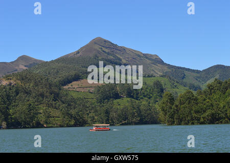Ein Boot am Kundala See bei Munnar mit Bäumen und Bergen im Hintergrund Stockfoto