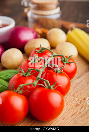 Frische Bio-Tomaten mit Gemüse auf Holzbrett. Potatoes,Onion,Sauce.Spices,Basil Stockfoto