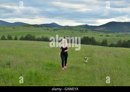 Joggen in der Natur an bewölkten Tag, während ihr Hund neben ihr läuft Frau Stockfoto