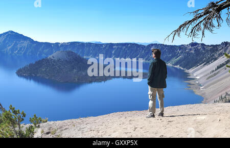 Kaukasischen Jüngling stehend betrachten Kratersee und den Wizard Island, die Hände in den Hosentaschen casual Dressing Stockfoto