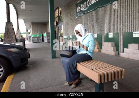 Muslimische Frau trägt einen Hijab, funktioniert ihr Handy auf einer Bank außerhalb Menards. St Paul Minnesota MN USA Stockfoto