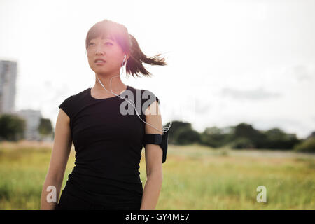 Schuss der junge Frau in Sportkleidung im Stadtpark am sonnigen Tag im Freien stehen und wegsehen. Chinesische weibliche Läufer bereit für Stockfoto
