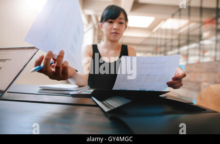 Schuss von Frau sitzt an ihrem Schreibtisch und Dokumente durchlaufen. Asiatische Geschäftsfrau mit Papierkram im Büro. Stockfoto