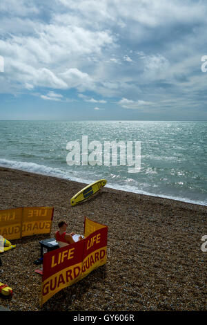 Bademeister am Strand von Brighton, Sussex, Vereinigtes Kingdon diensthabenden. Bewachen Sie Windschutz zu und Surfen Sie niederwarf sitzen am Strand, umgeben von Leben Stockfoto