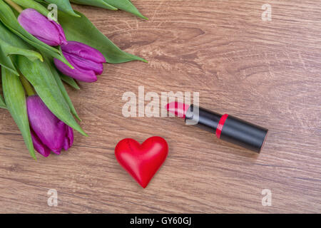 Lippenstift, rote Herzen und violette Tulpen auf einem hölzernen Hintergrund Stockfoto