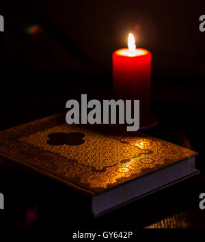 Buch und Kerze auf einem Tisch in der Dunkelheit Stockfoto