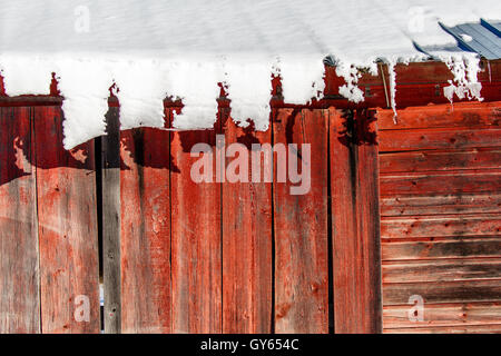 Schnee auf dem Blechdach einer roten Scheune langsam nach unten gleiten. Stockfoto