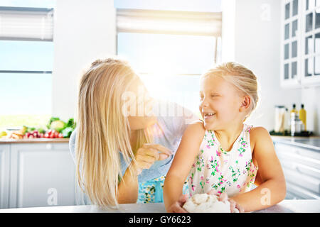 Liebevolle Mutter lehrt ihre süße kleine Tochter zu backen, lachen und scherzen, wie sie den Teig für Teig knetet Stockfoto