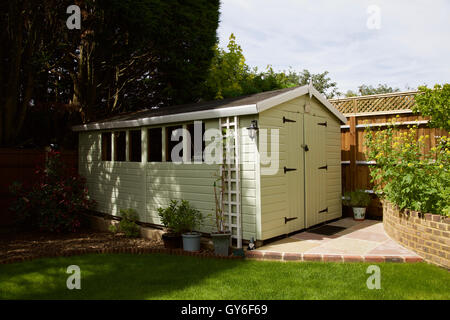 Großen blass grün gemalte Hütte in s Rückseite Garten mit Rasen und Zaun mit Spalier und Pflasterung und Pitch Dach Stockfoto